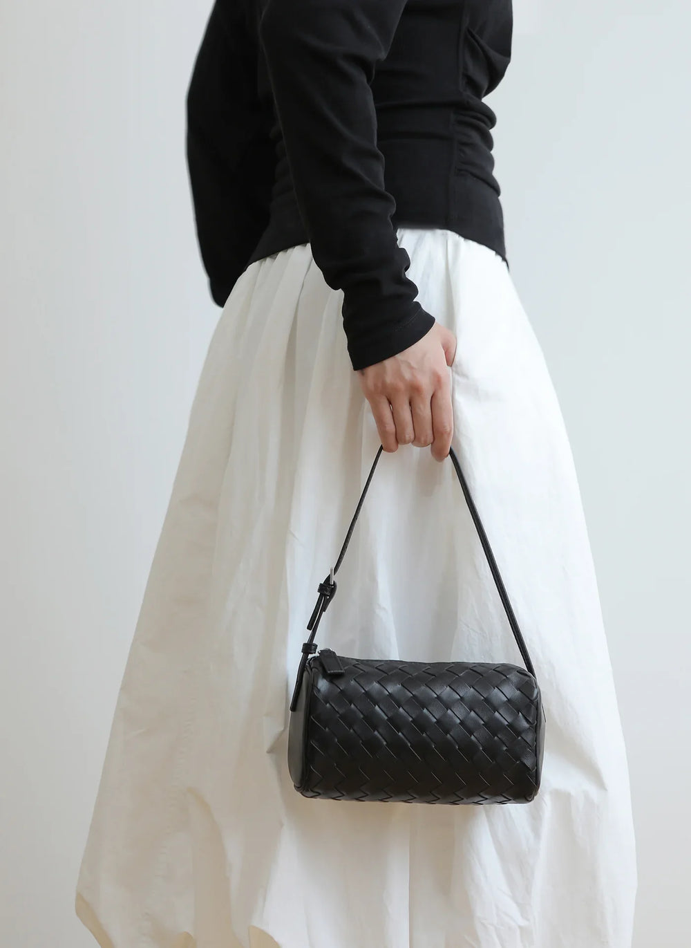 Woman holding a black woven lambskin leather mini Boston bag with shoulder strap.