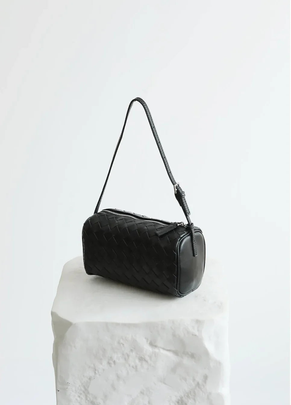 Black lambskin leather woven mini Boston bag with shoulder strap on white stone block