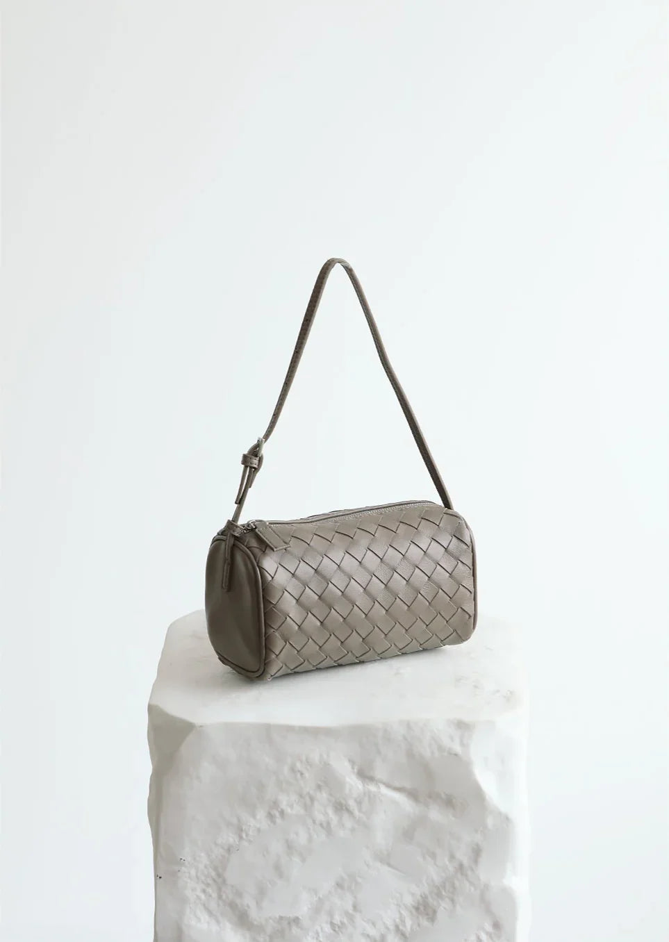 Taupe woven lambskin leather mini Boston bag with shoulder strap on white display pedestal