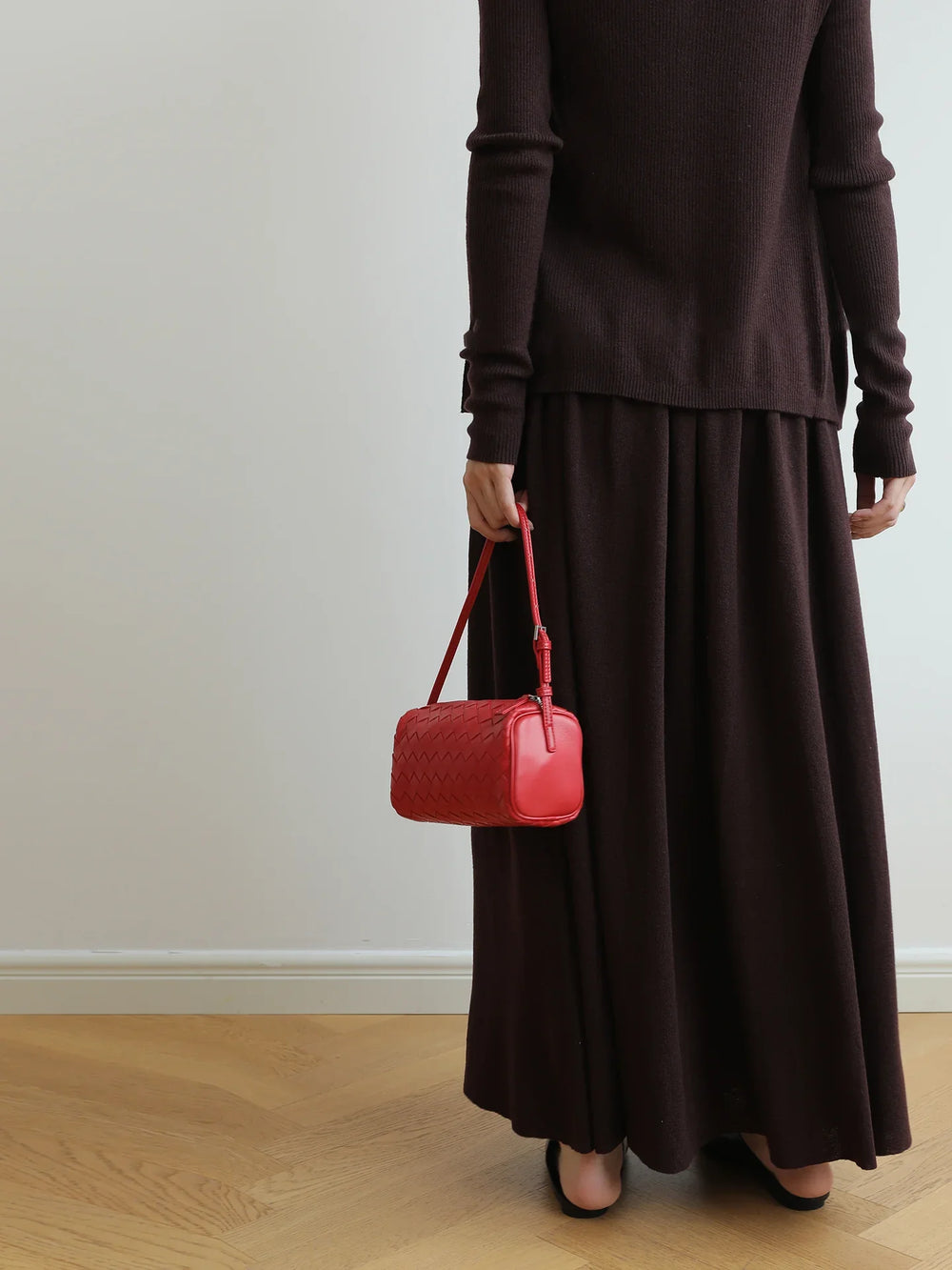 Woman holding a small red woven lambskin leather shoulder bag, wearing a dark brown dress