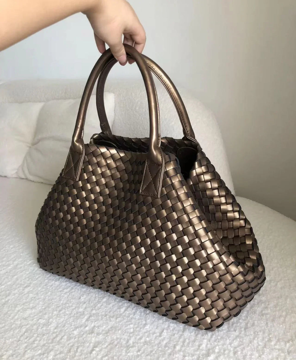 Hand holding large handwoven vegan leather tote bag in metallic onyx on a bed