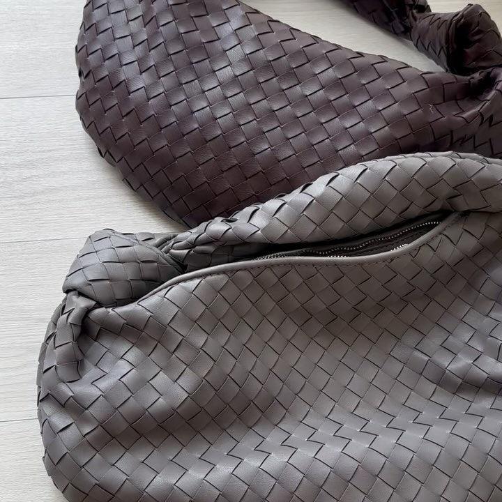 Two large woven lambskin leather handbags with knotted handles on a light wood surface.