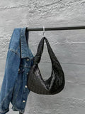 Black woven lambskin leather knotted dumpling handbag hanging beside denim jacket on rack