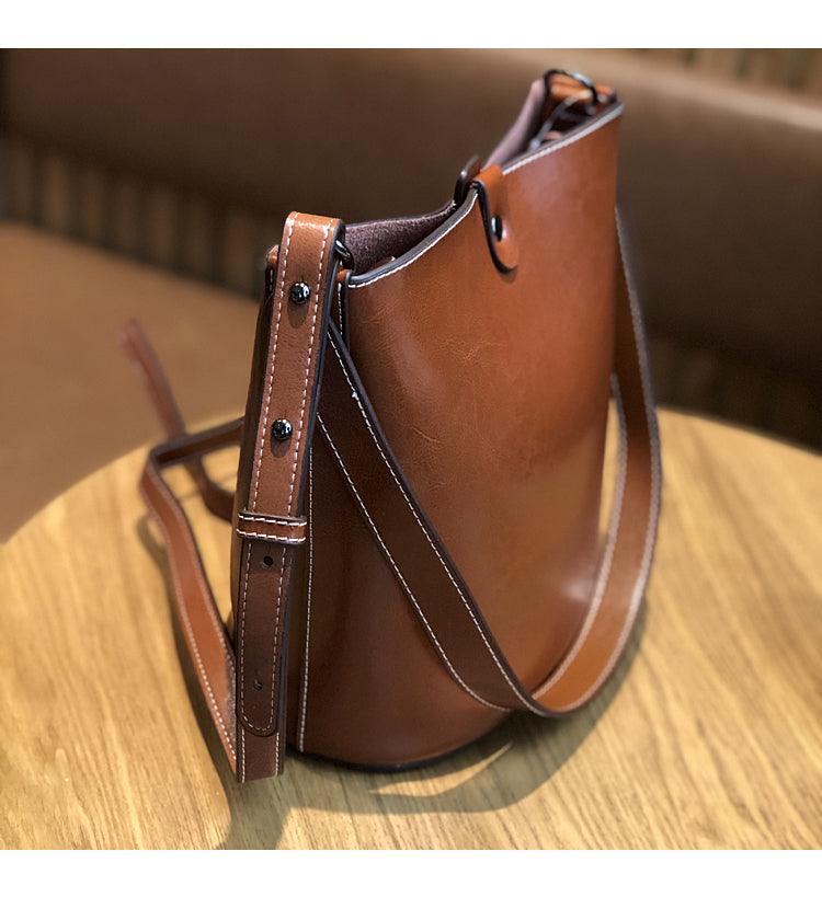 Brown leather bucket bag with adjustable shoulder strap on wooden table