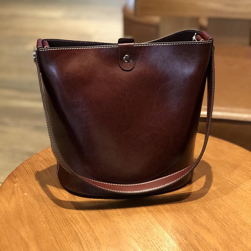 Brown leather bucket bag with adjustable shoulder strap on wooden table