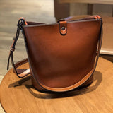 Brown leather bucket bag with crossbody strap on wooden table, minimalist design
