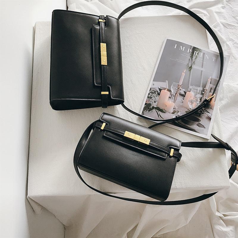 Minimalist black leather crossbody handbags with gold hardware on a white cloth, next to a magazine.