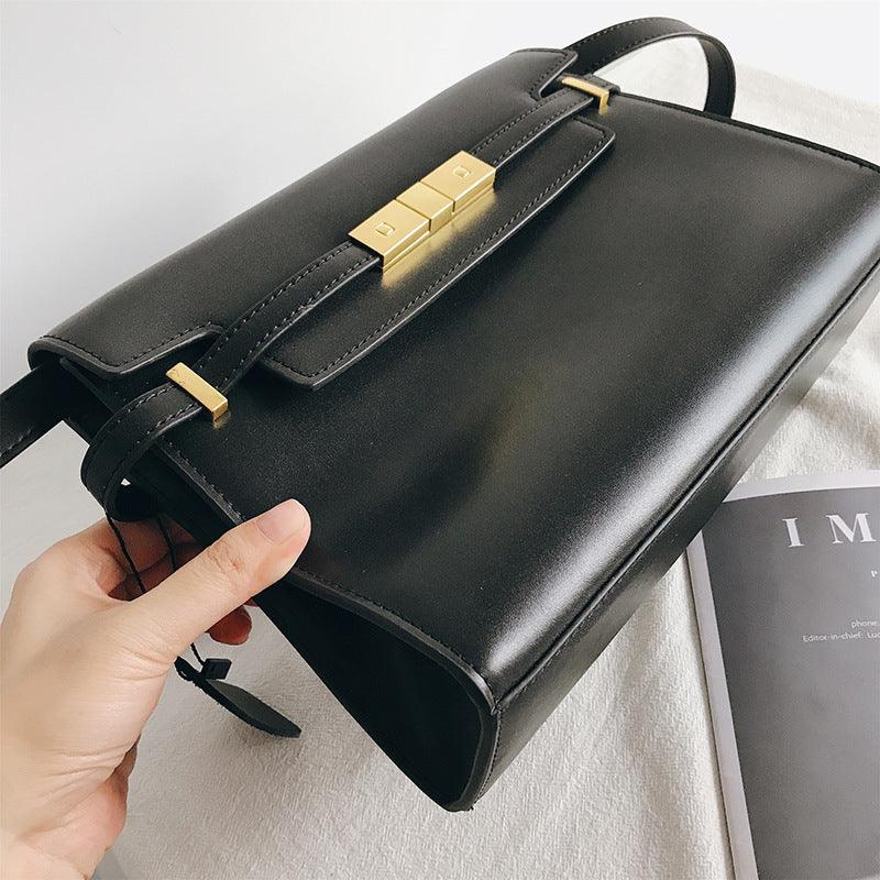 Minimal black leather crossbody bag with gold hardware, modern design, on white surface