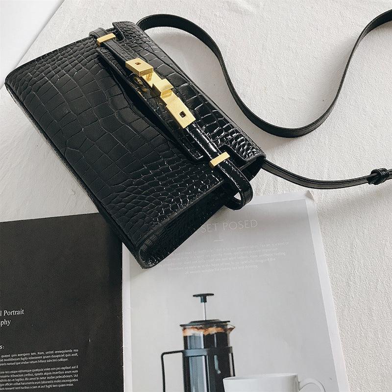 Black leather crossbody bag with crocodile pattern and gold hardware on a white surface
