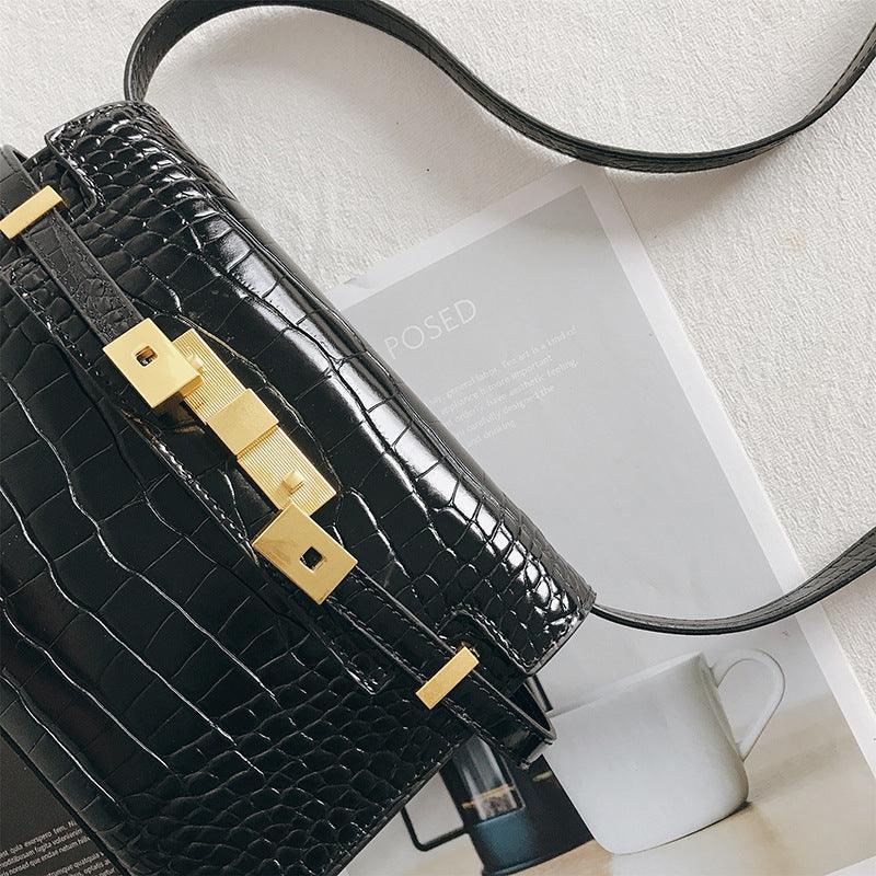 Black crocodile-embossed leather crossbody bag with gold hardware on a white surface.