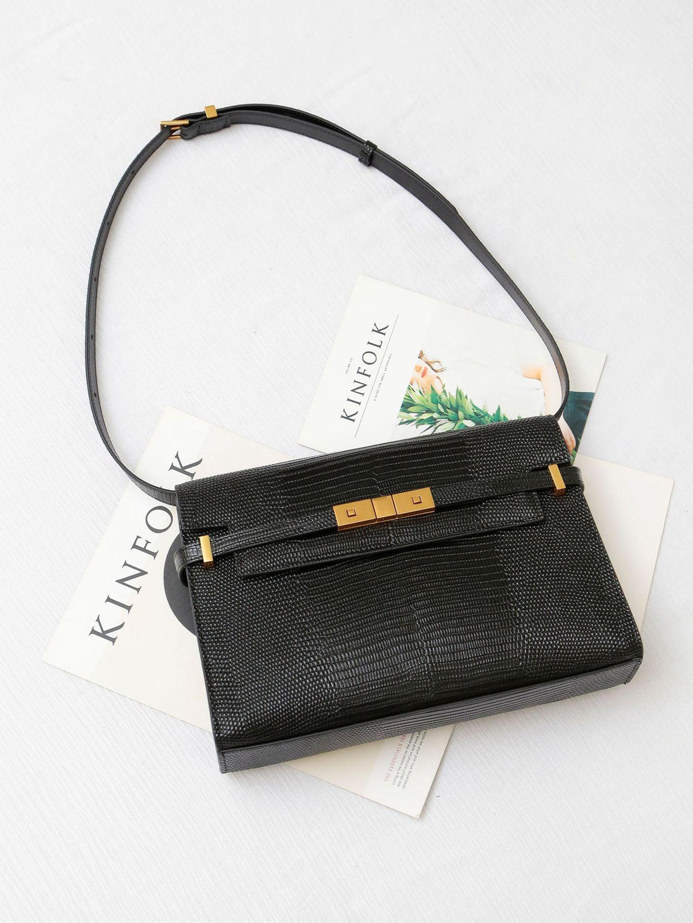 Black leather crossbody bag with gold hardware on white surface and magazines