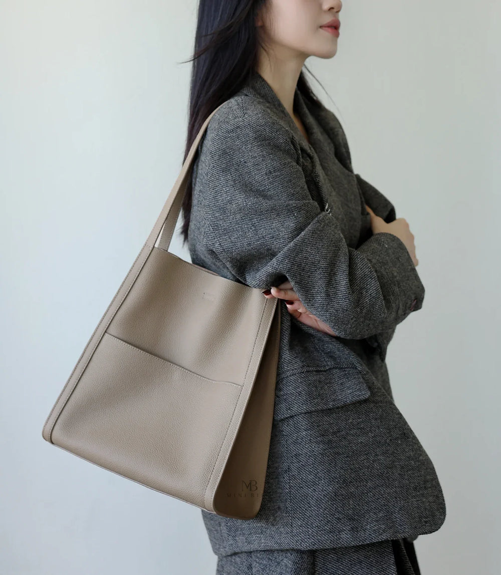 Woman wearing a minimalist taupe leather tote bag with shoulder strap and exterior pocket