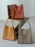 Three minimalist cowhide leather tote bags in tan, camel, and beige on a modern chair.