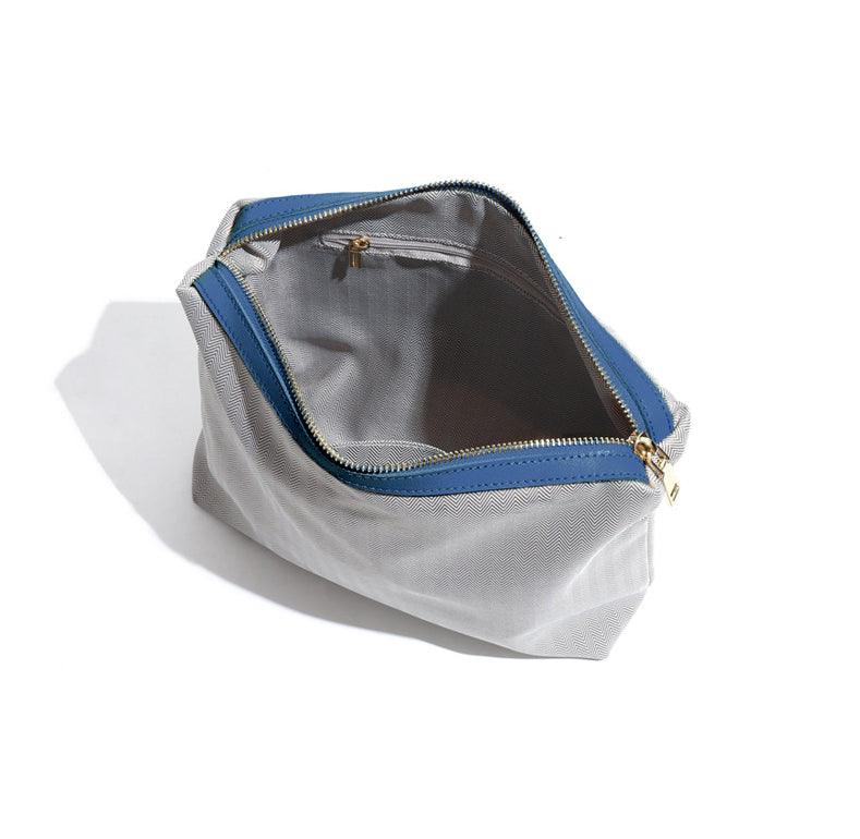 Gray fabric pouch with blue leather trim, gold zipper, and interior pocket, open view