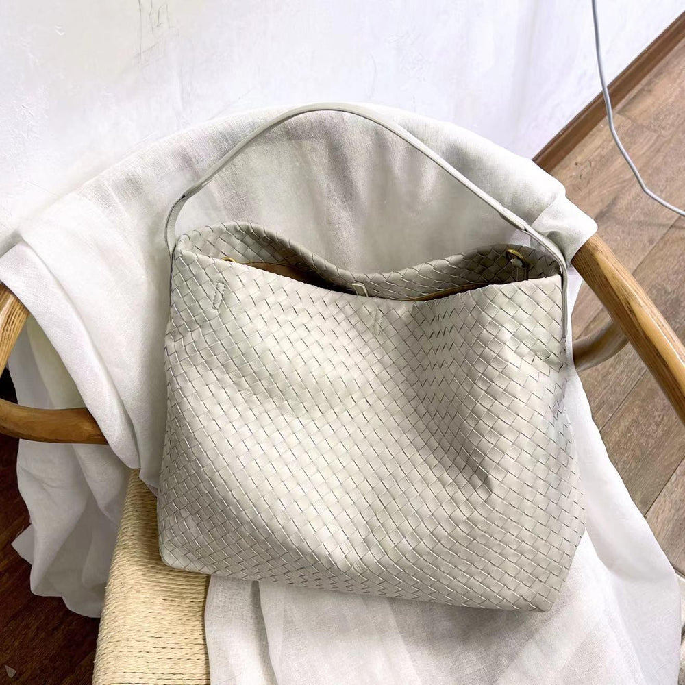 Beige woven lambskin leather tote bag with a single handle on a wooden chair.
