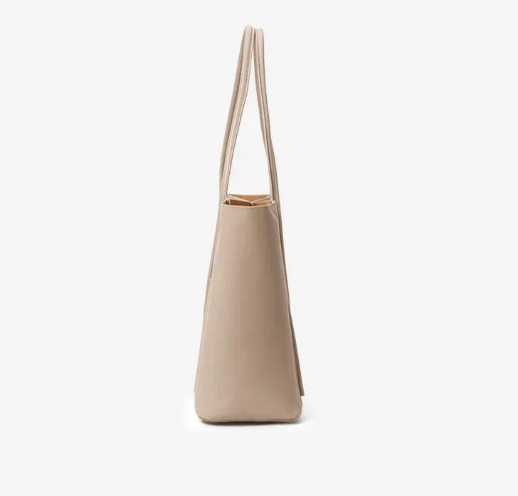 Side view of a minimalist beige genuine leather tote handbag with double top handles.