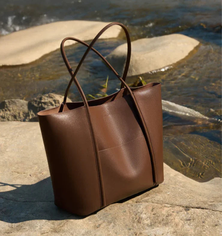 Minimalist brown genuine leather tote bag with top handles on a rock by riverside
