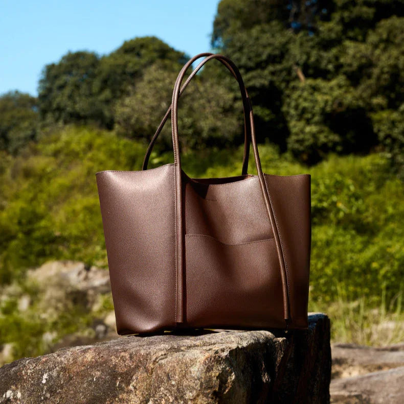 Minimalist genuine leather tote bag with top handles, shown outdoors on a rock