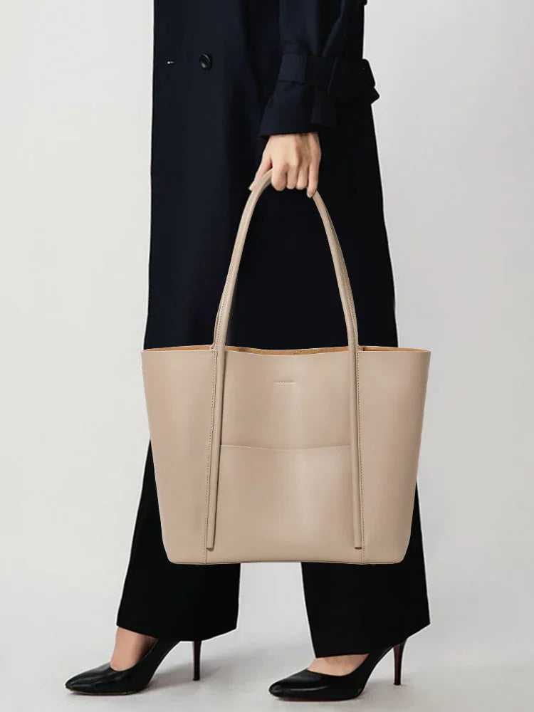 Minimalist beige genuine leather tote handbag with top handles, held by woman in black coat