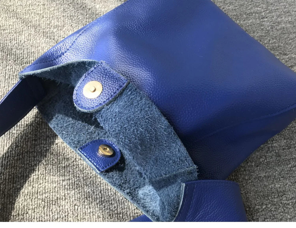 Minimalist blue pebbled cowhide leather bucket bag with wide shoulder strap and snap closure