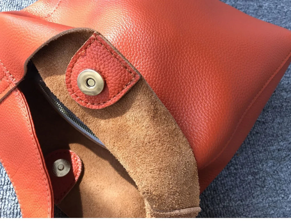 Close-up of an orange pebbled cowhide leather bucket bag with snap closure on fabric background