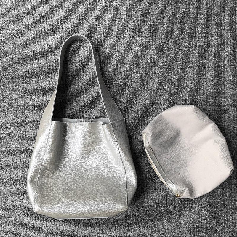 Minimalist pebbled cowhide leather bucket bag with wide shoulder strap and removable pouch on grey surface
