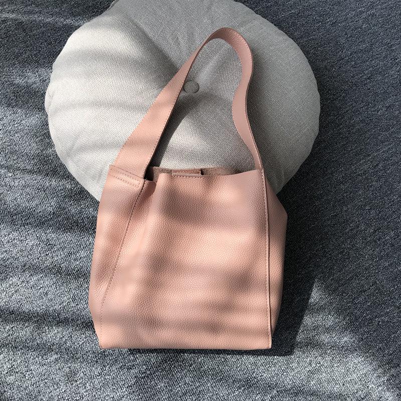 Minimalist pebbled cowhide leather bucket bag with wide shoulder strap on a cushion