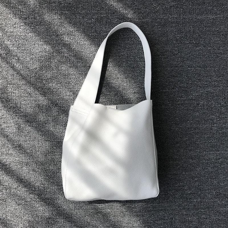 Minimalist white pebbled cowhide leather bucket bag with wide shoulder strap on gray fabric