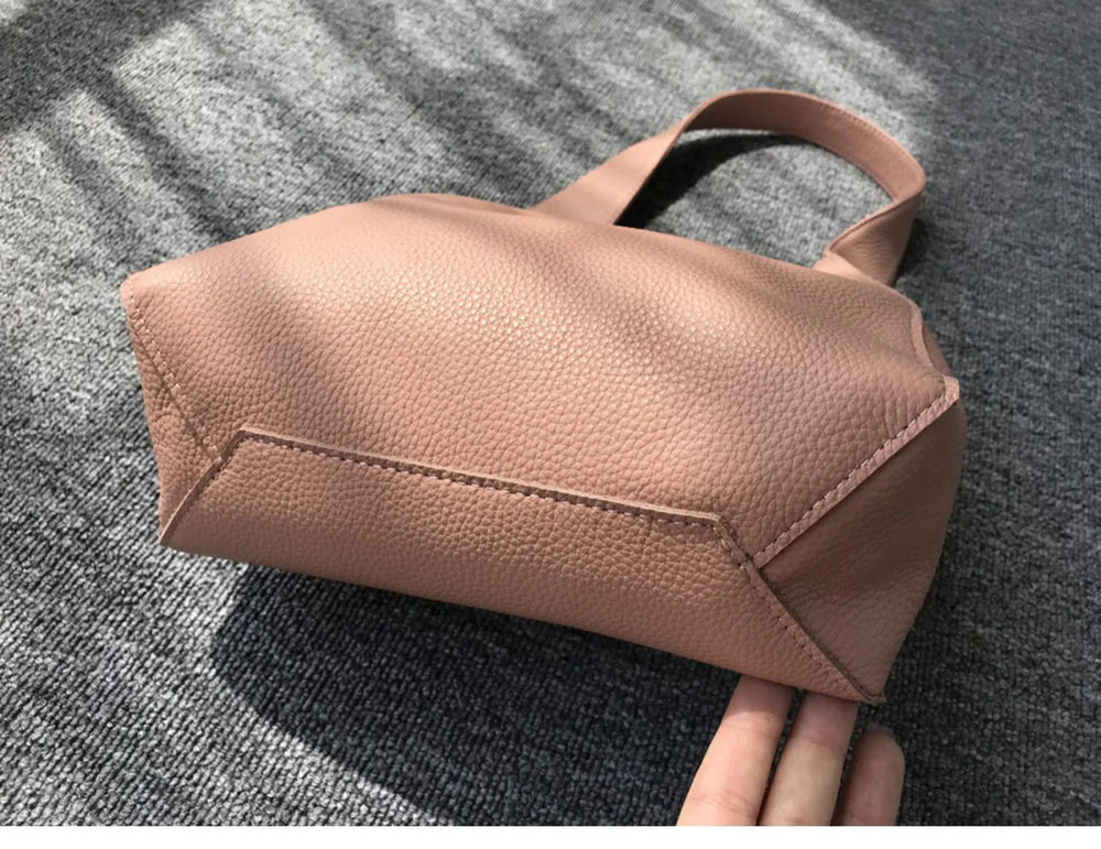 Minimalist pebbled cowhide leather bucket bag with wide shoulder strap on grey carpet