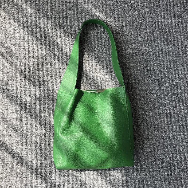 Minimalist green pebbled cowhide leather bucket bag with wide shoulder strap on grey background