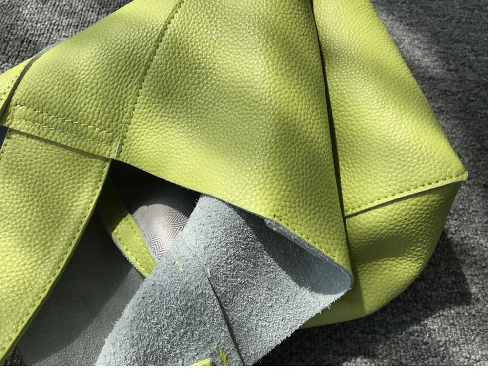 Minimalist green pebbled cowhide leather bucket bag with wide shoulder strap on fabric surface