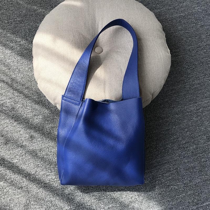 Minimalist blue pebbled cowhide leather bucket bag with wide shoulder strap on cushion