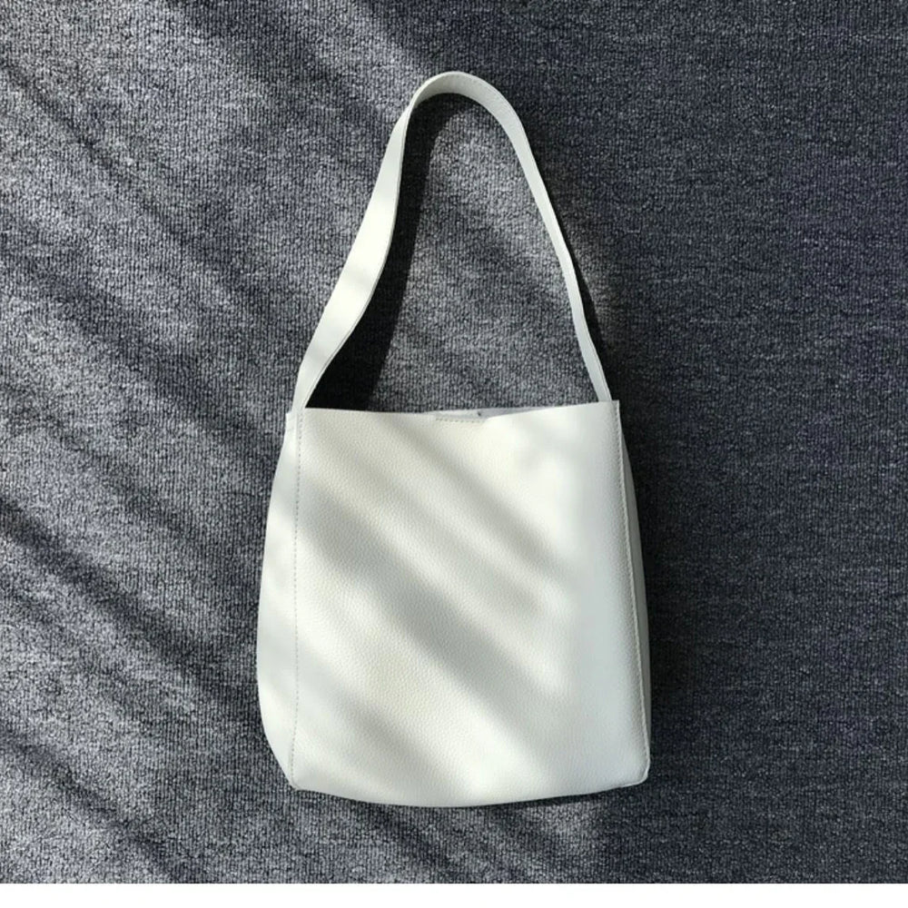 Minimalist white pebbled cowhide leather bucket bag with wide shoulder strap on grey fabric