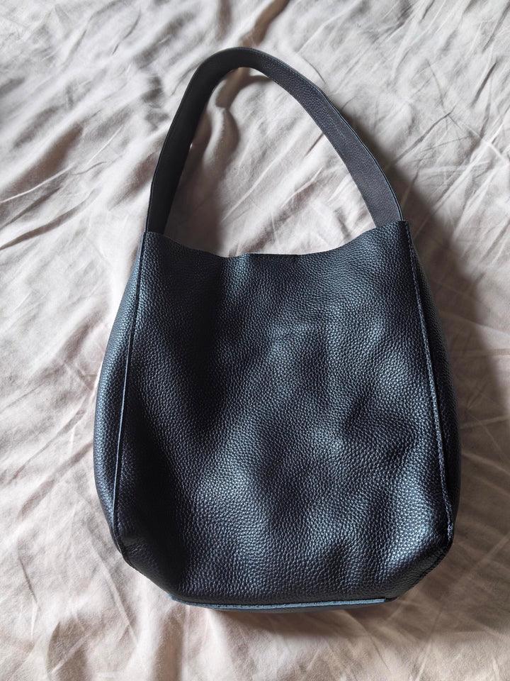 Black leather shoulder bag with textured surface on a beige fabric background