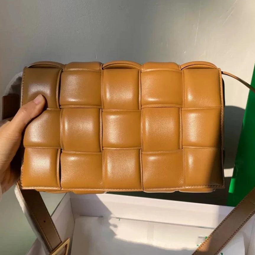 Hand holding a tan woven leather crossbody bag with padded square pattern