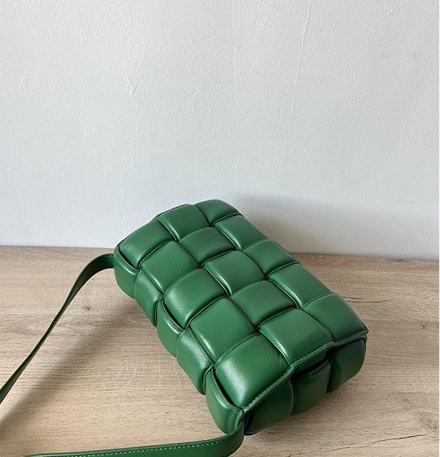 Green woven leather crossbody bag with padded texture on a wooden surface