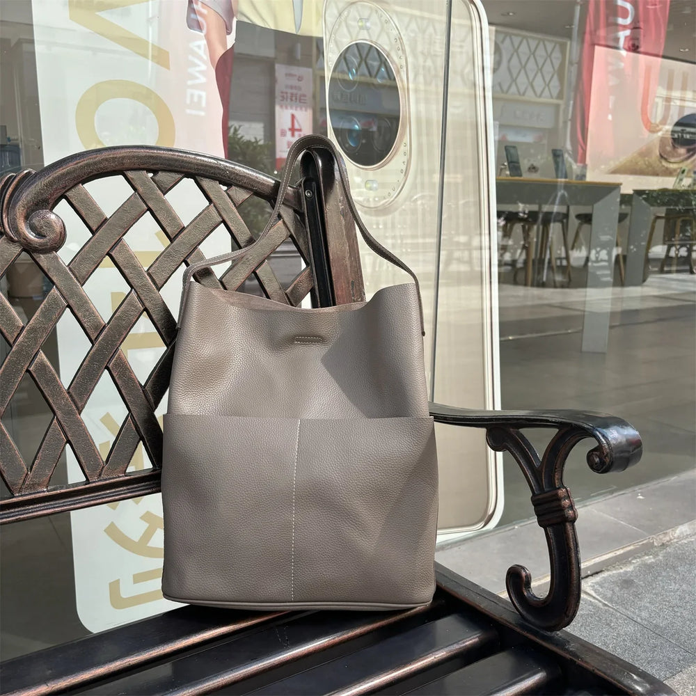 Taupe cowhide leather tote bag with front pockets on a bench outdoors
