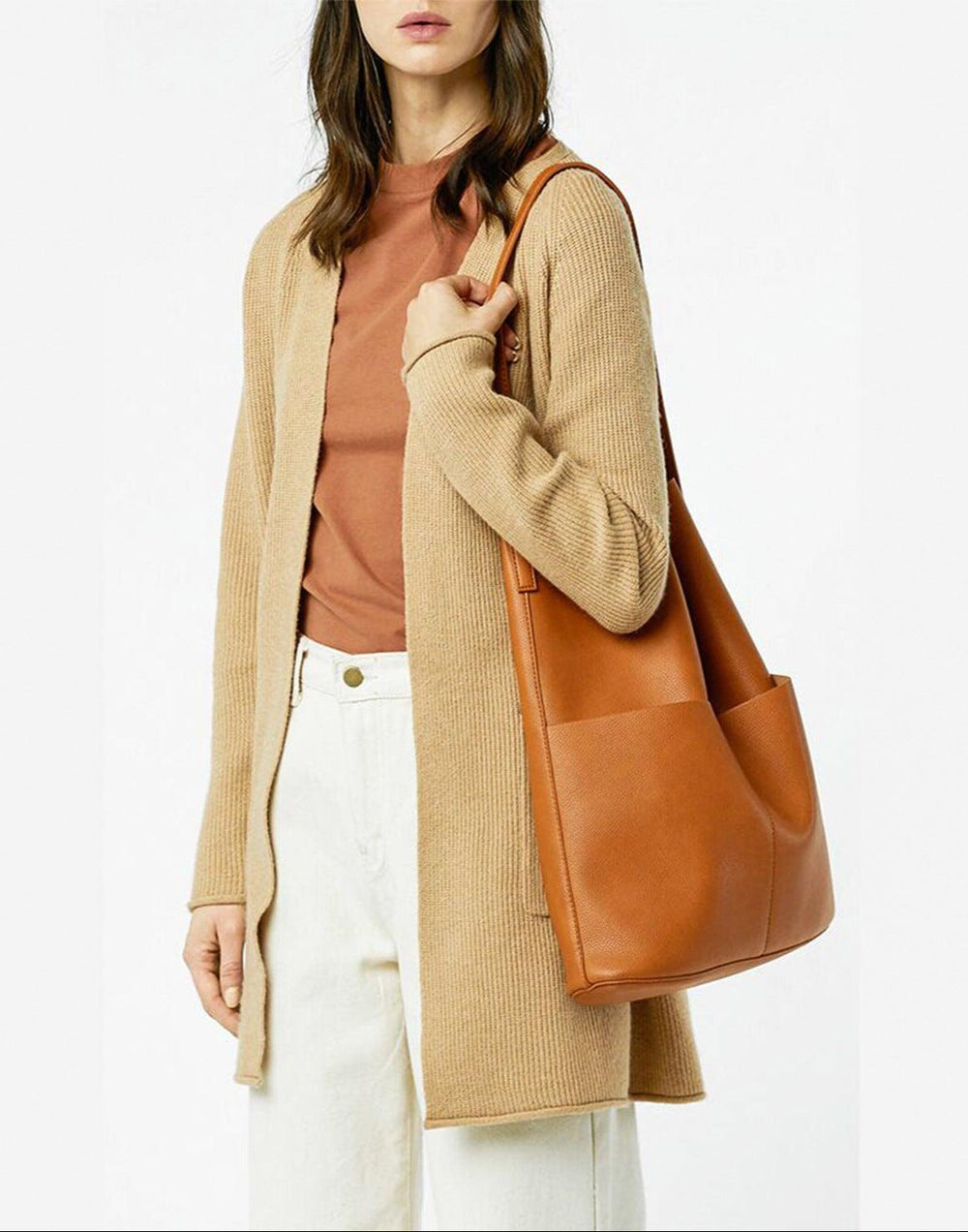 Woman wearing a tan leather tote bag with two front pockets and a minimalist design