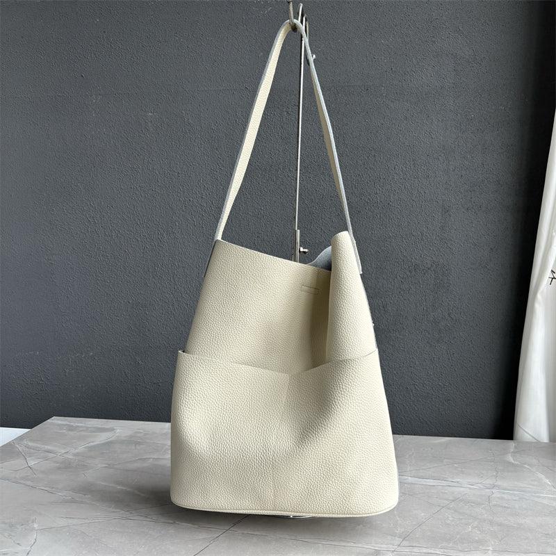 Cream cowhide leather tote bag with two front pockets, minimalist design, on marble surface