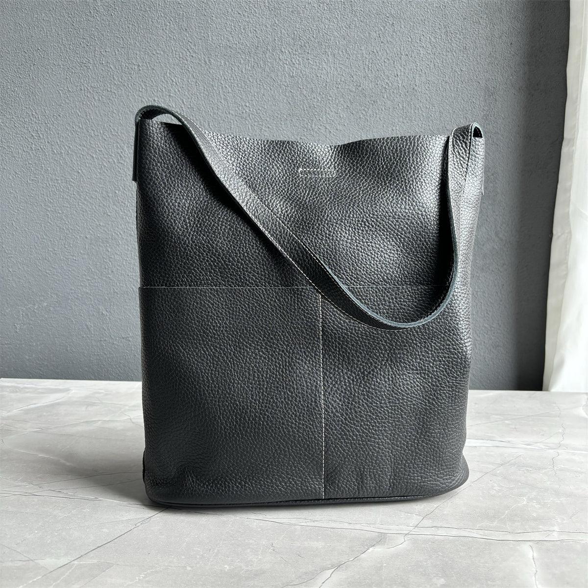 Black cowhide leather tote bag with two front pockets, minimalist design, on marble surface