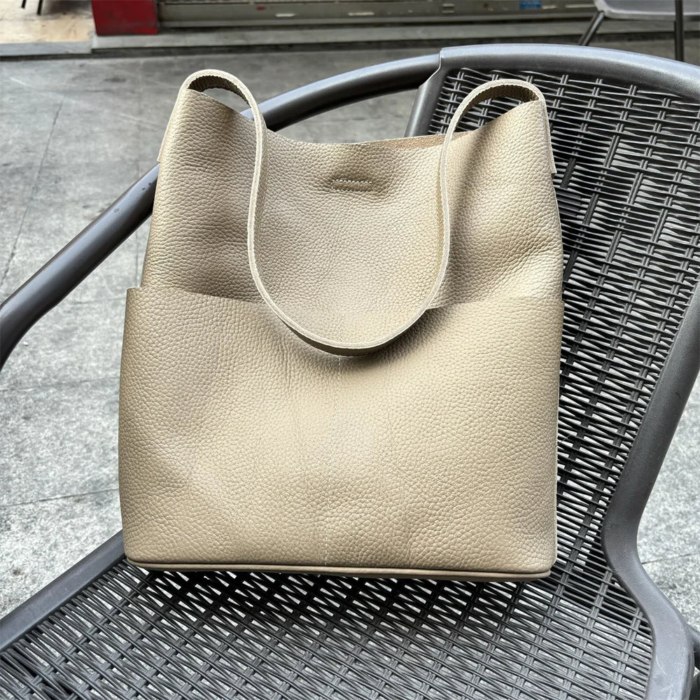 Soft tan cowhide leather tote bag with two front pockets on a wicker chair outdoors