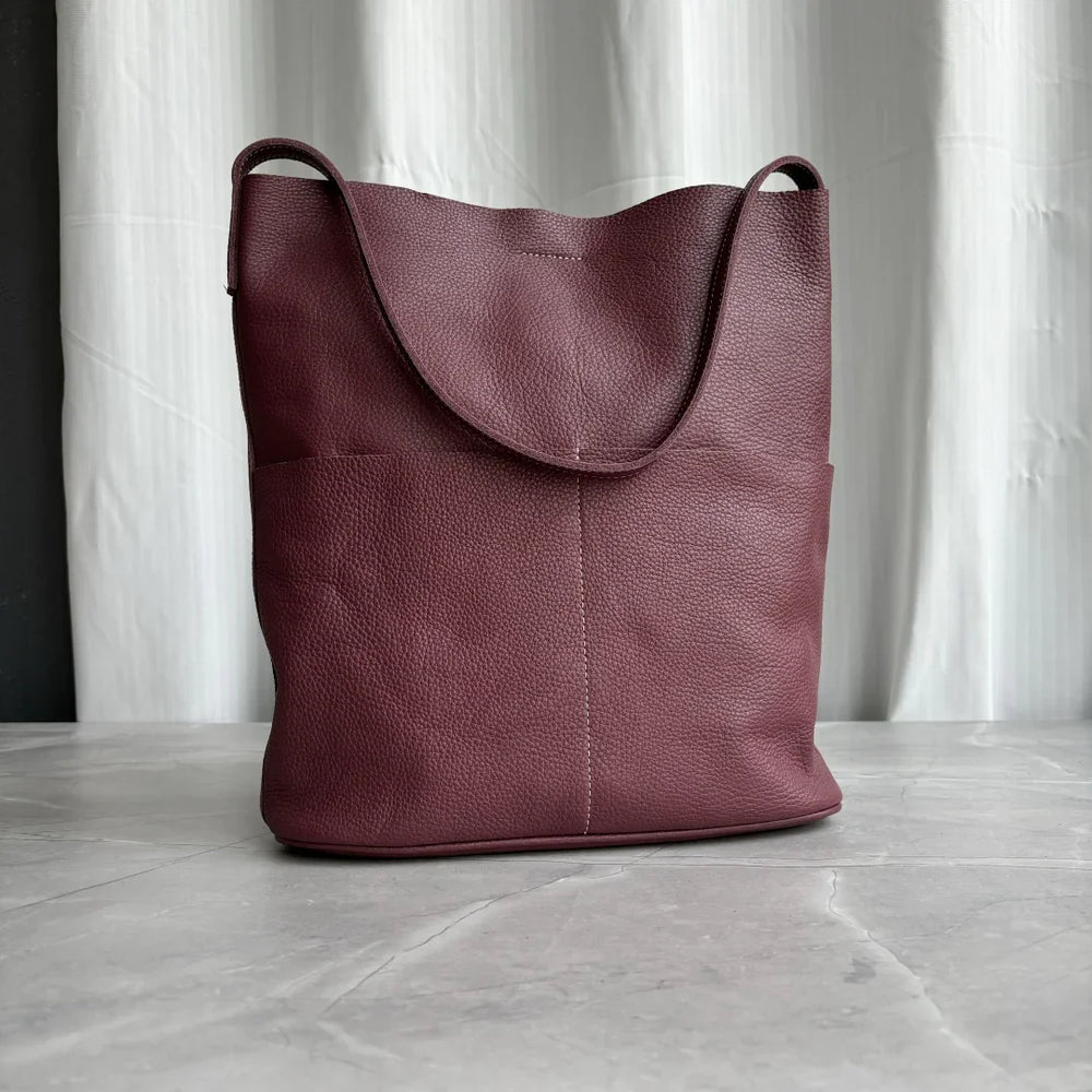 Brown cowhide leather tote bag with two front pockets on marble surface, minimalist design