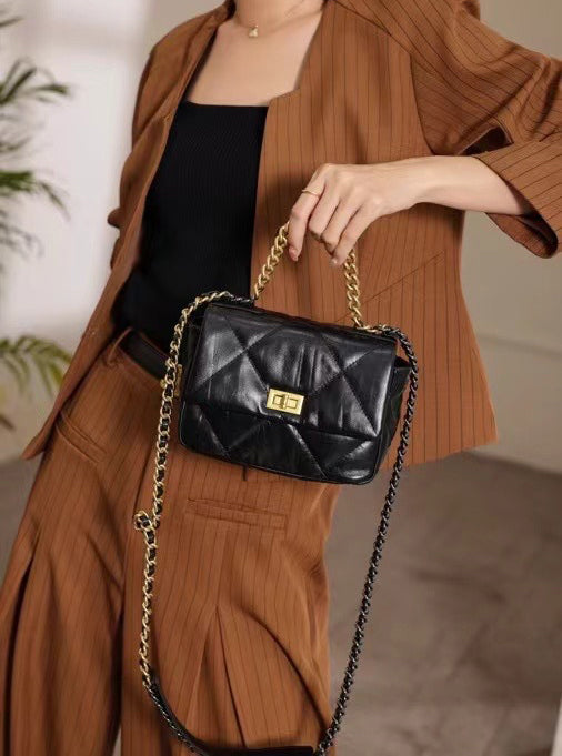 Woman holding black quilted leather shoulder bag with gold chain strap and gold lock clasp