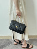 Black quilted leather shoulder bag with gold chain strap, held by woman in light dress