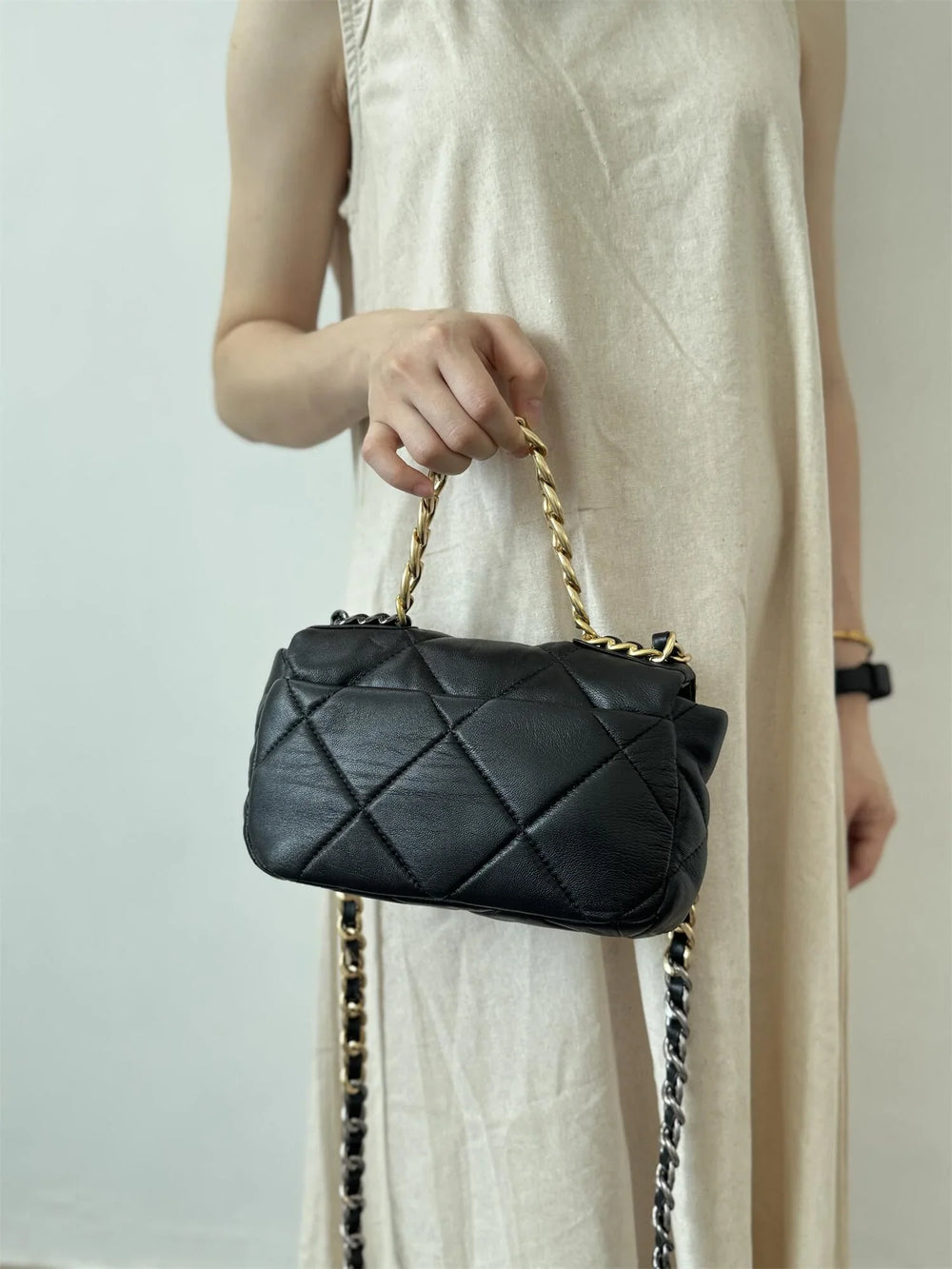 Woman holding a black quilted genuine leather shoulder bag with gold chain handle