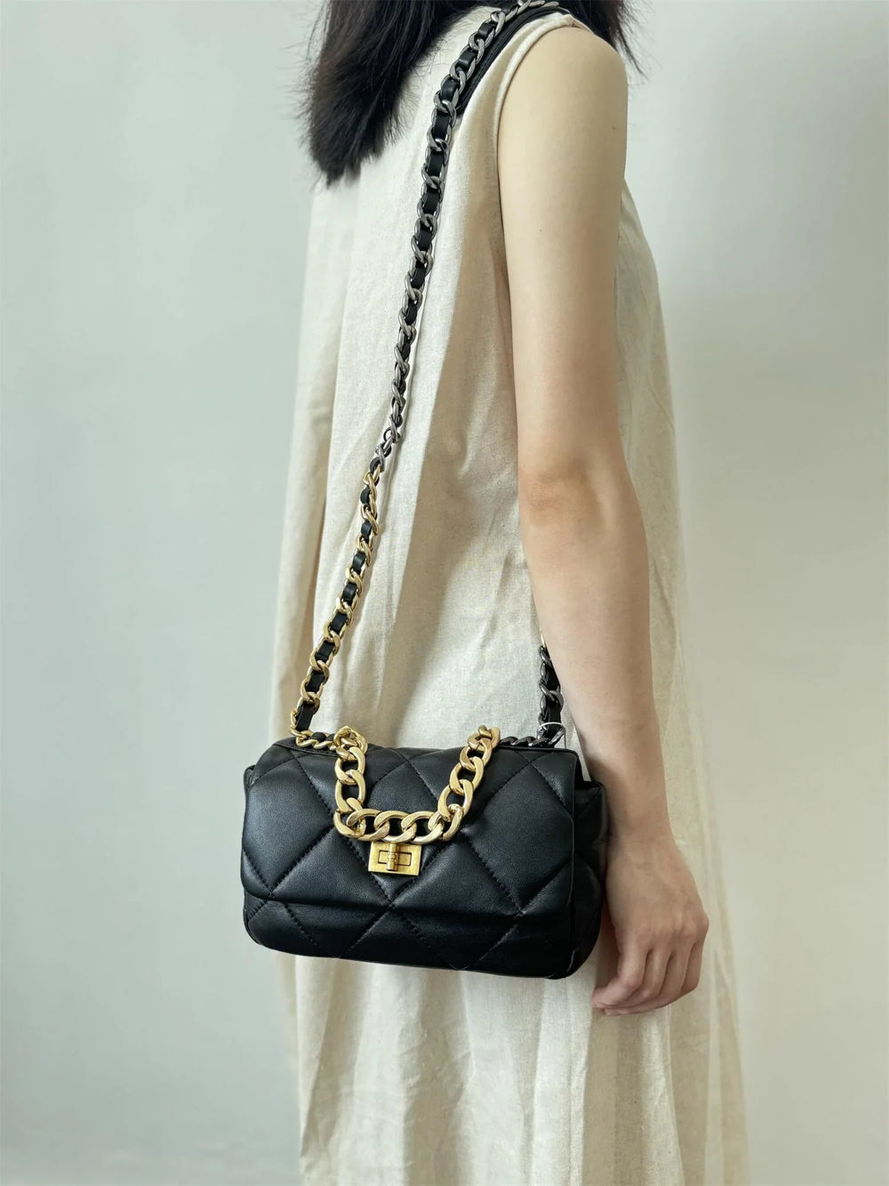 Woman wearing a black quilted leather shoulder bag with gold chain and turn-lock clasp