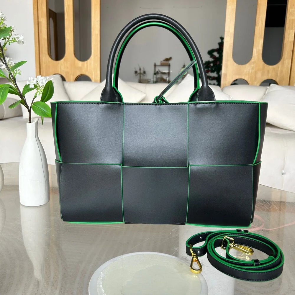 Large black quilted leather tote bag with green trim and detachable shoulder strap on table