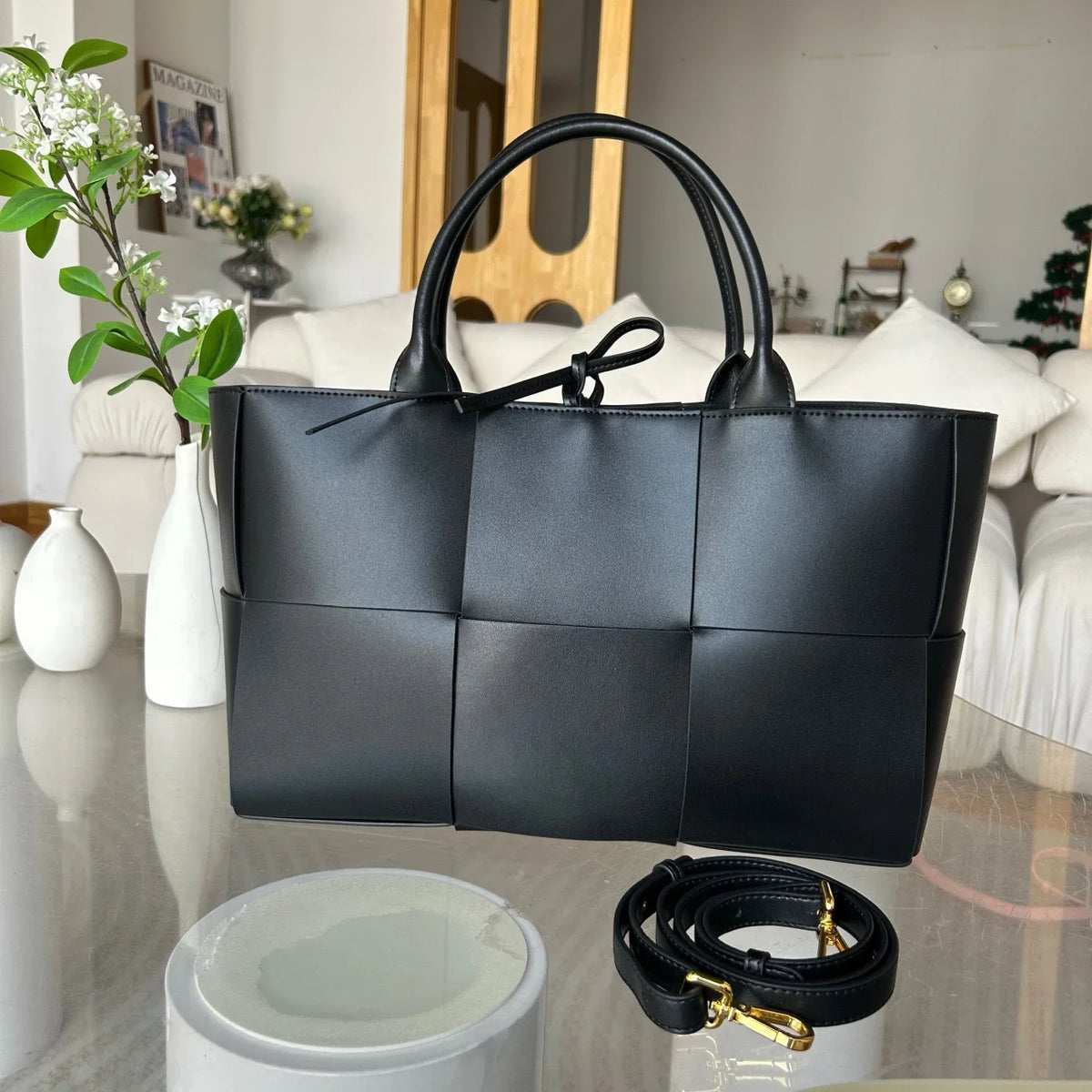 Large black woven leather tote bag with top handles and detachable strap on a table