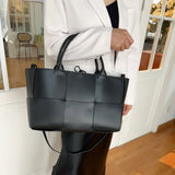 Woman holding a large black quilted leather tote bag with top handles and shoulder strap