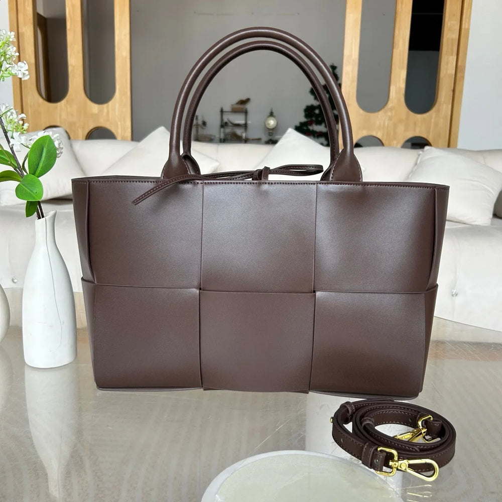 Large brown quilted leather tote bag with top handles and detachable shoulder strap on a table.